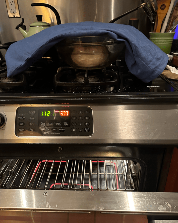 a dough in a bowl under a heating pad, sitting on a stove.